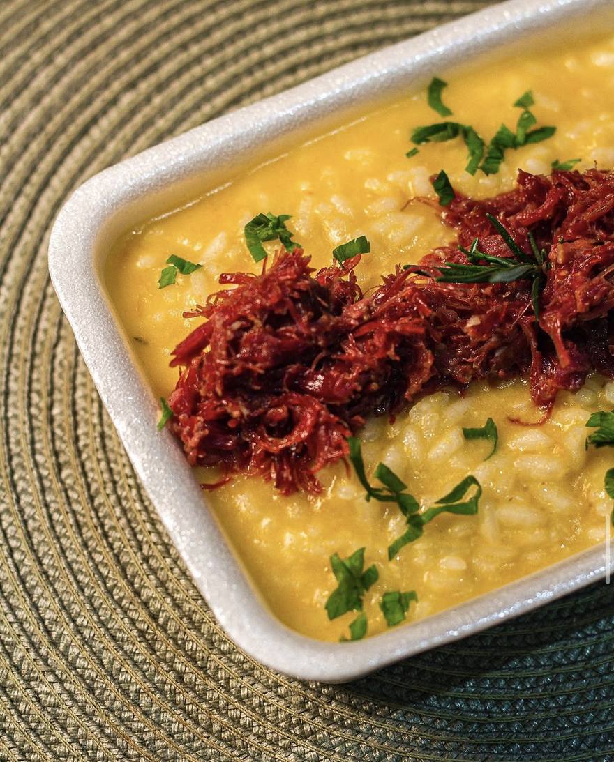 Risoto cremoso com carne desfiada, servido em embalagem de delivery